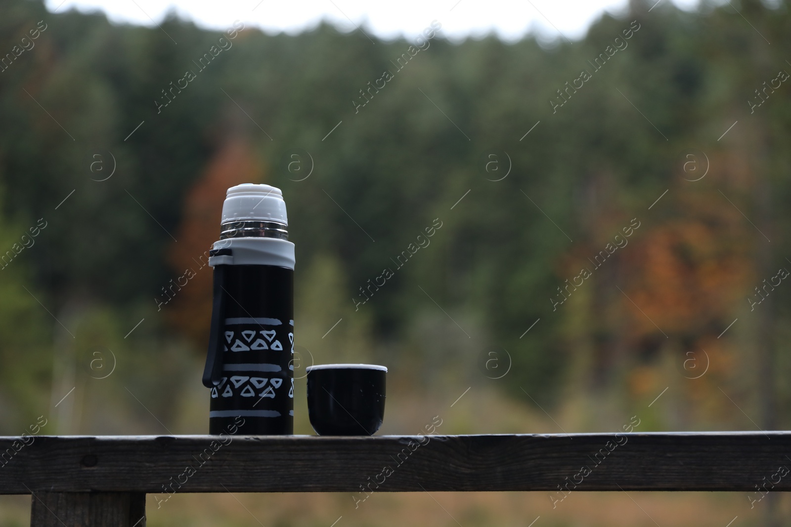 Photo of Black thermos and cup lid on handrail outdoors, space for text