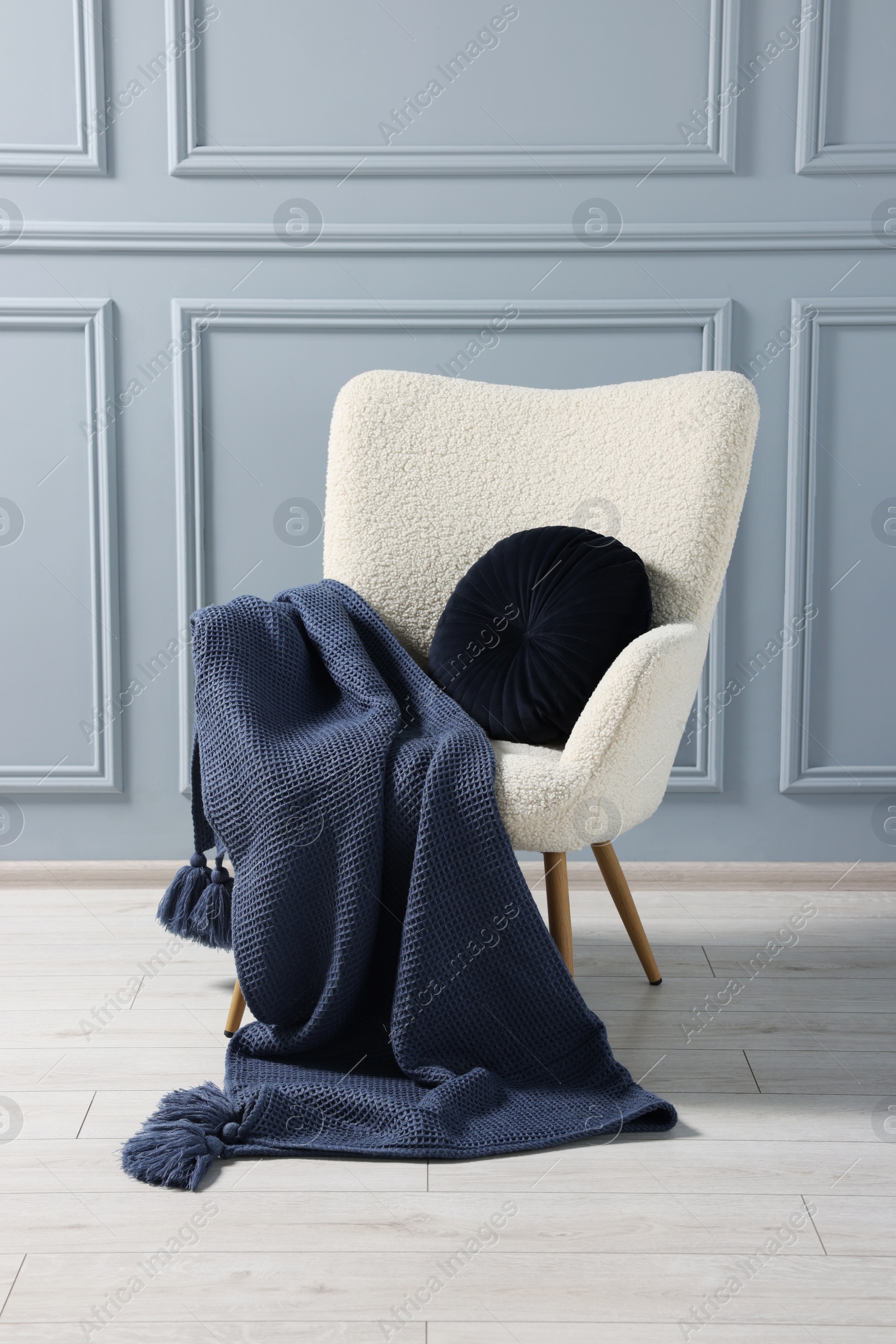 Photo of Comfortable armchair with blanket and pillow near grey wall indoors