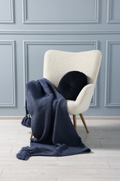 Photo of Comfortable armchair with blanket and pillow near grey wall indoors