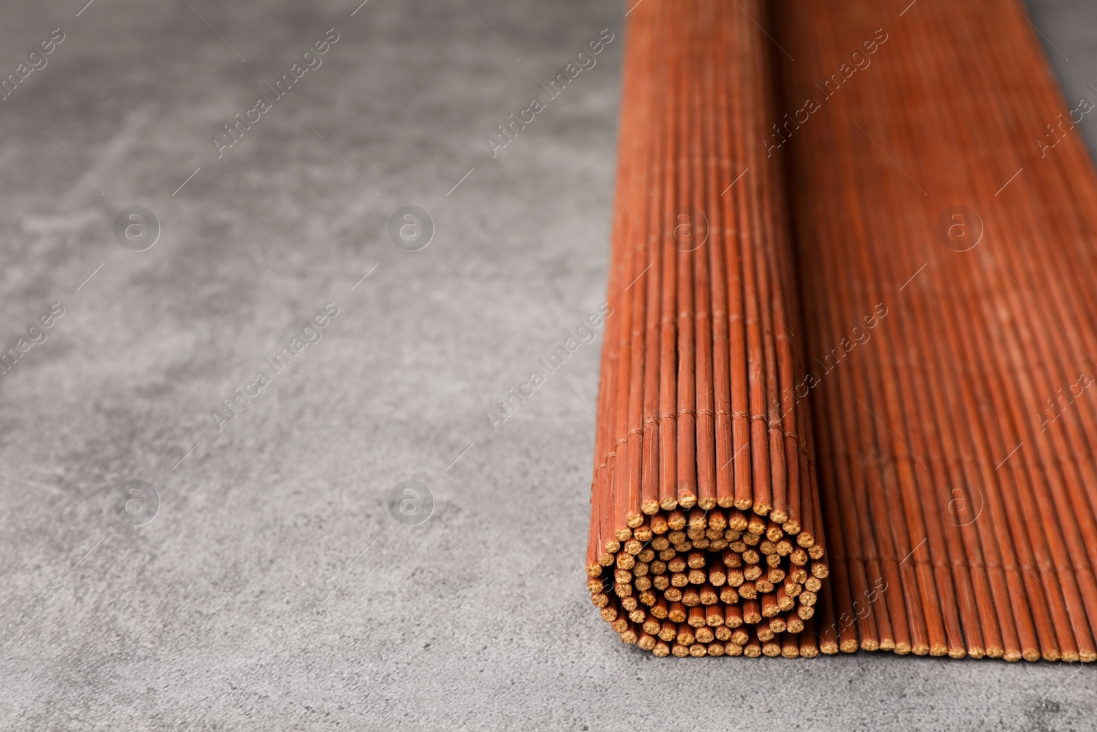 Photo of Rolled bamboo mat on grey table, closeup. Space for text