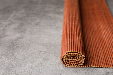 Photo of Rolled bamboo mat on grey table, closeup. Space for text
