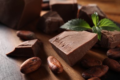 Pieces of tasty milk chocolate, mint and cocoa beans on wooden table, closeup