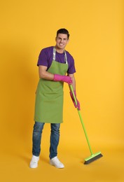 Photo of Man with green broom on orange background