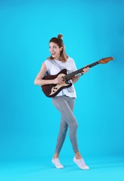 Young woman playing electric guitar on color background