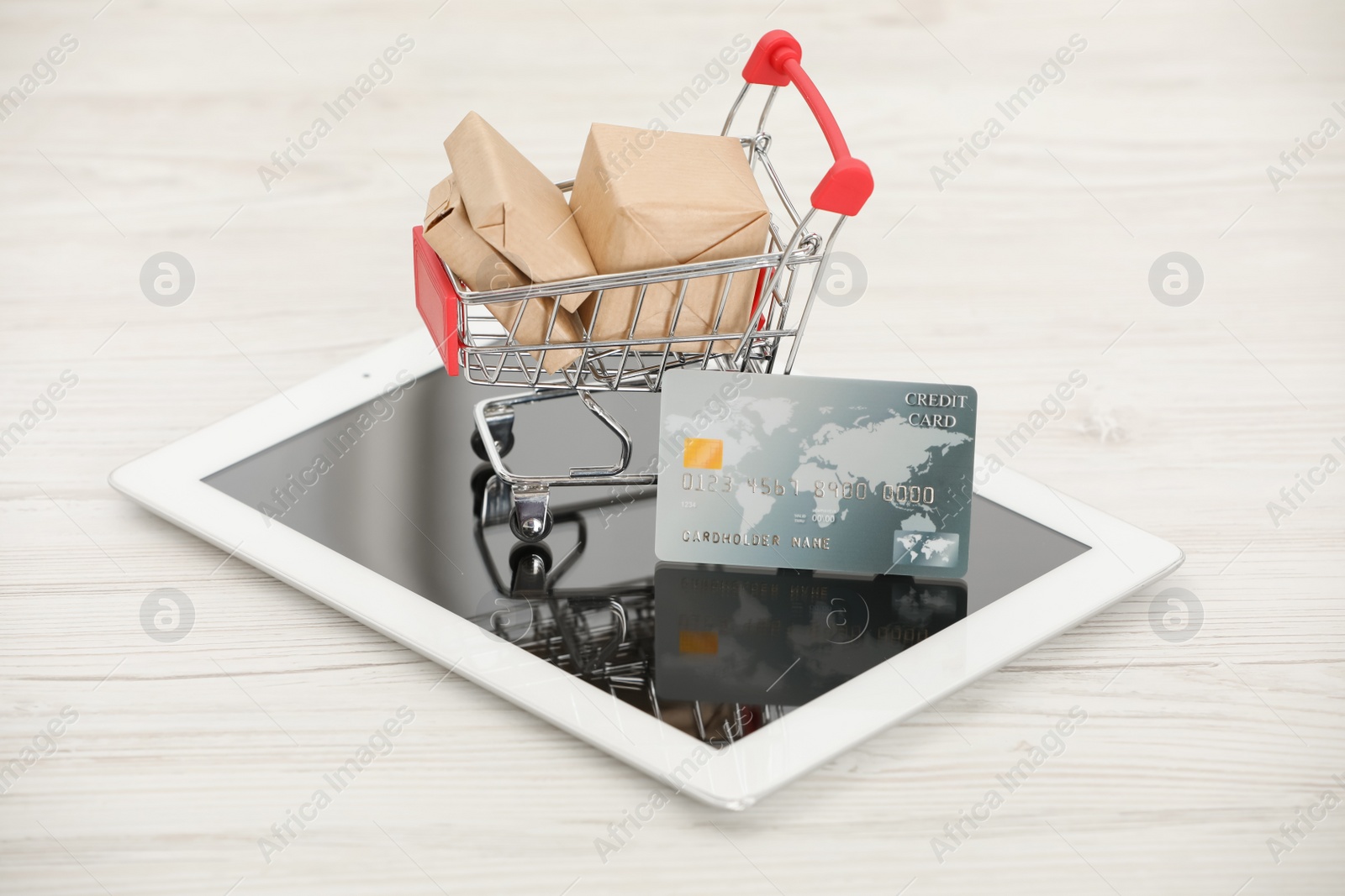 Photo of Online payment concept. Small shopping cart with bank card, boxes and tablet on white table