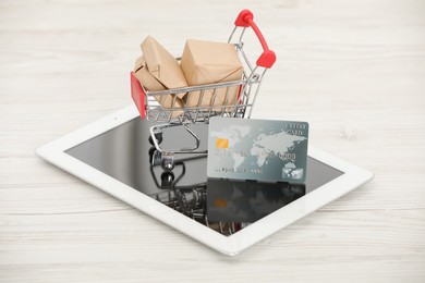 Online payment concept. Small shopping cart with bank card, boxes and tablet on white table