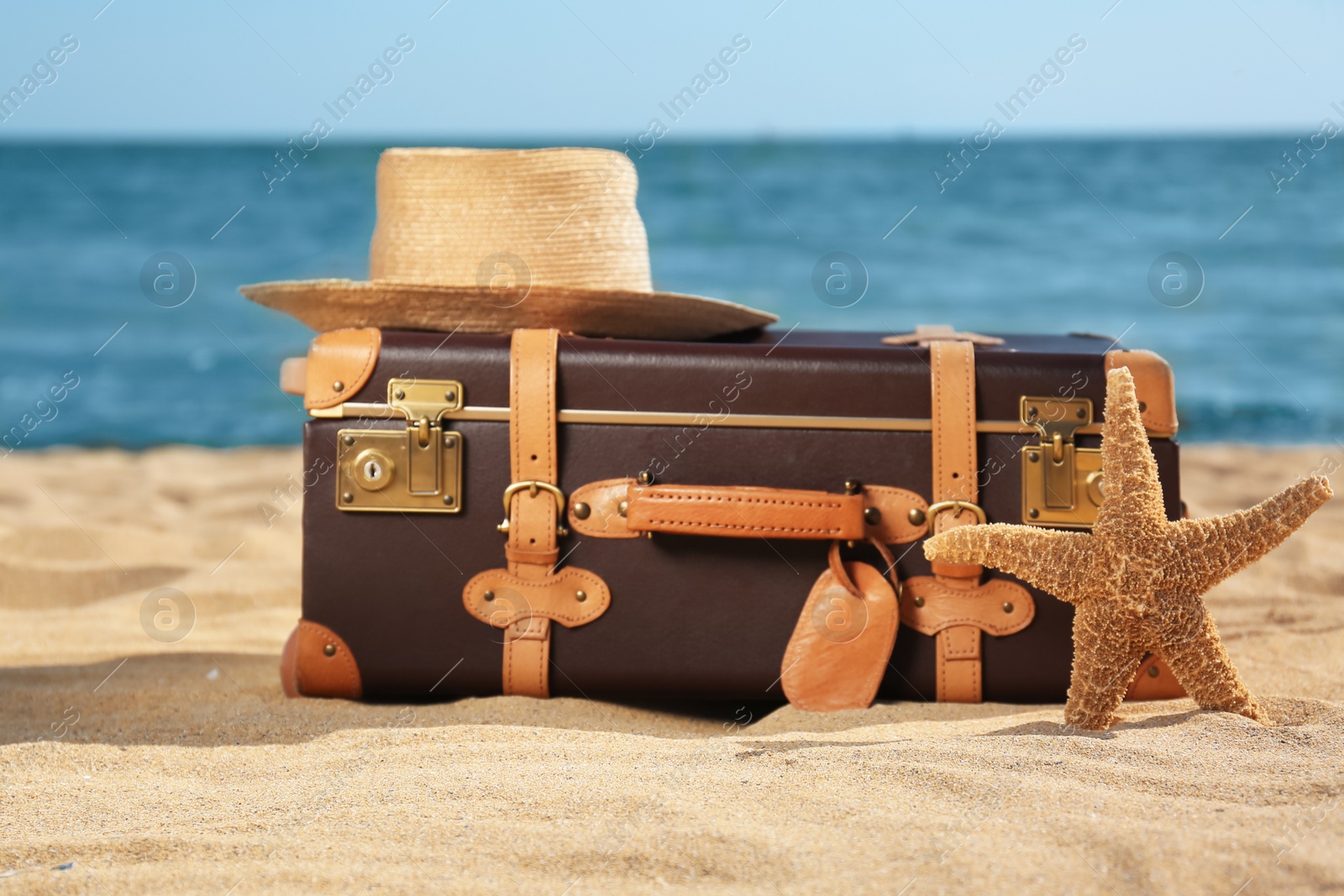 Photo of Suitcase, hat and starfish on sand near sea. Beach accessories