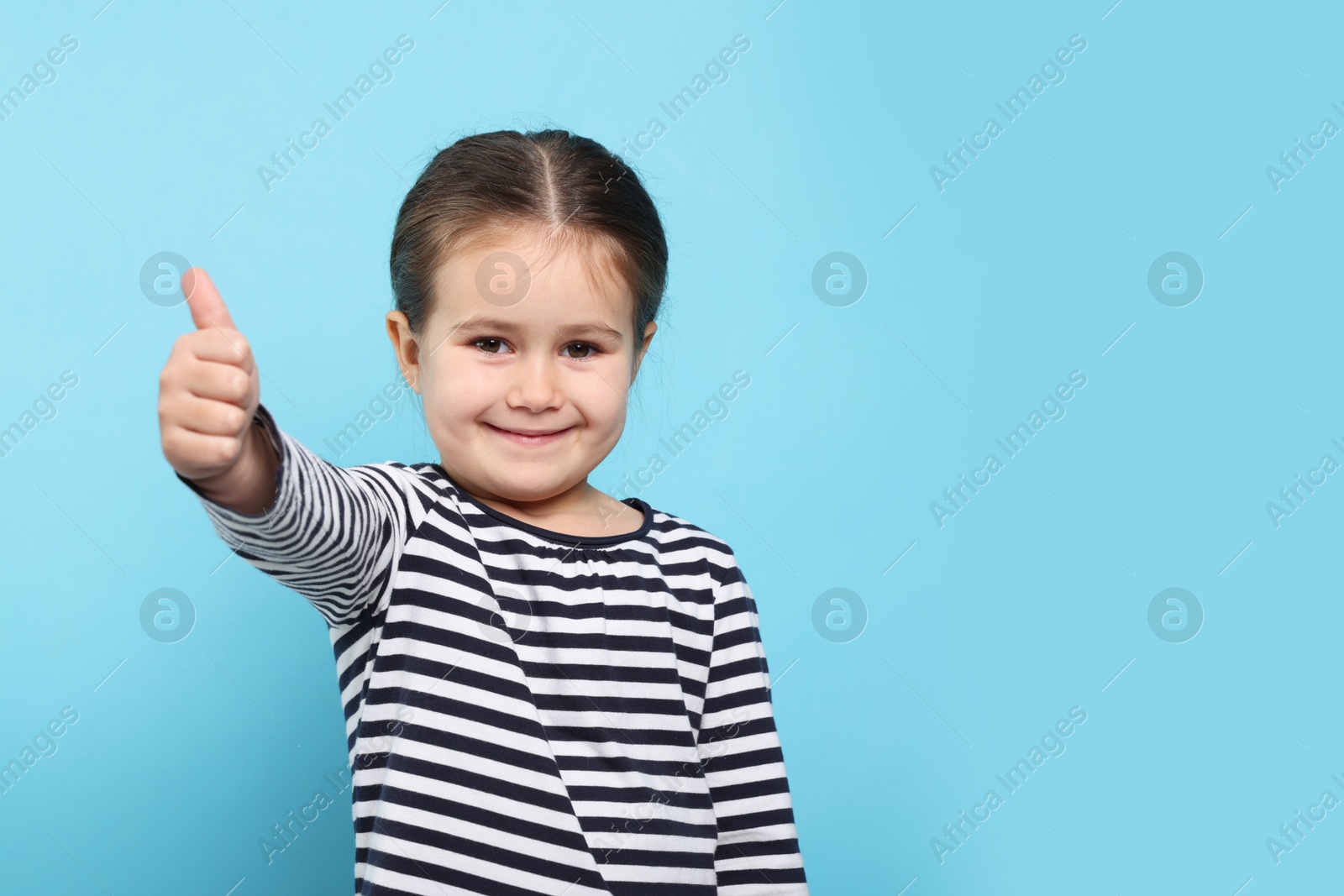 Photo of Happy girl showing thumbs up on light blue background. Space for text