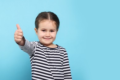 Photo of Happy girl showing thumbs up on light blue background. Space for text