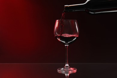 Photo of Pouring red wine from bottle into glass on dark background, space for text