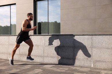 Young man running near building outdoors. Space for text