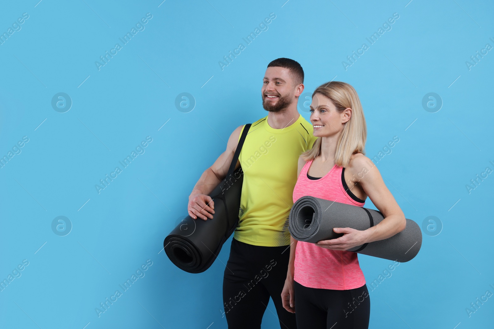 Photo of Athletic people with fitness mats on light blue background, space for text