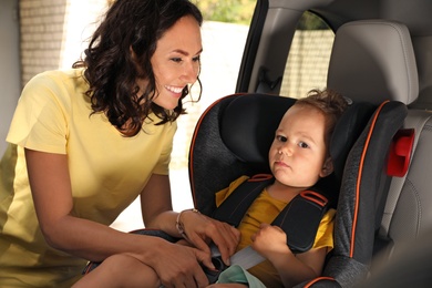 Mother fastening her son with car safety belt in child seat. Family vacation