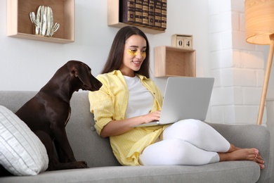 Young woman with eye patches working on laptop near her dog in living room. Home office concept