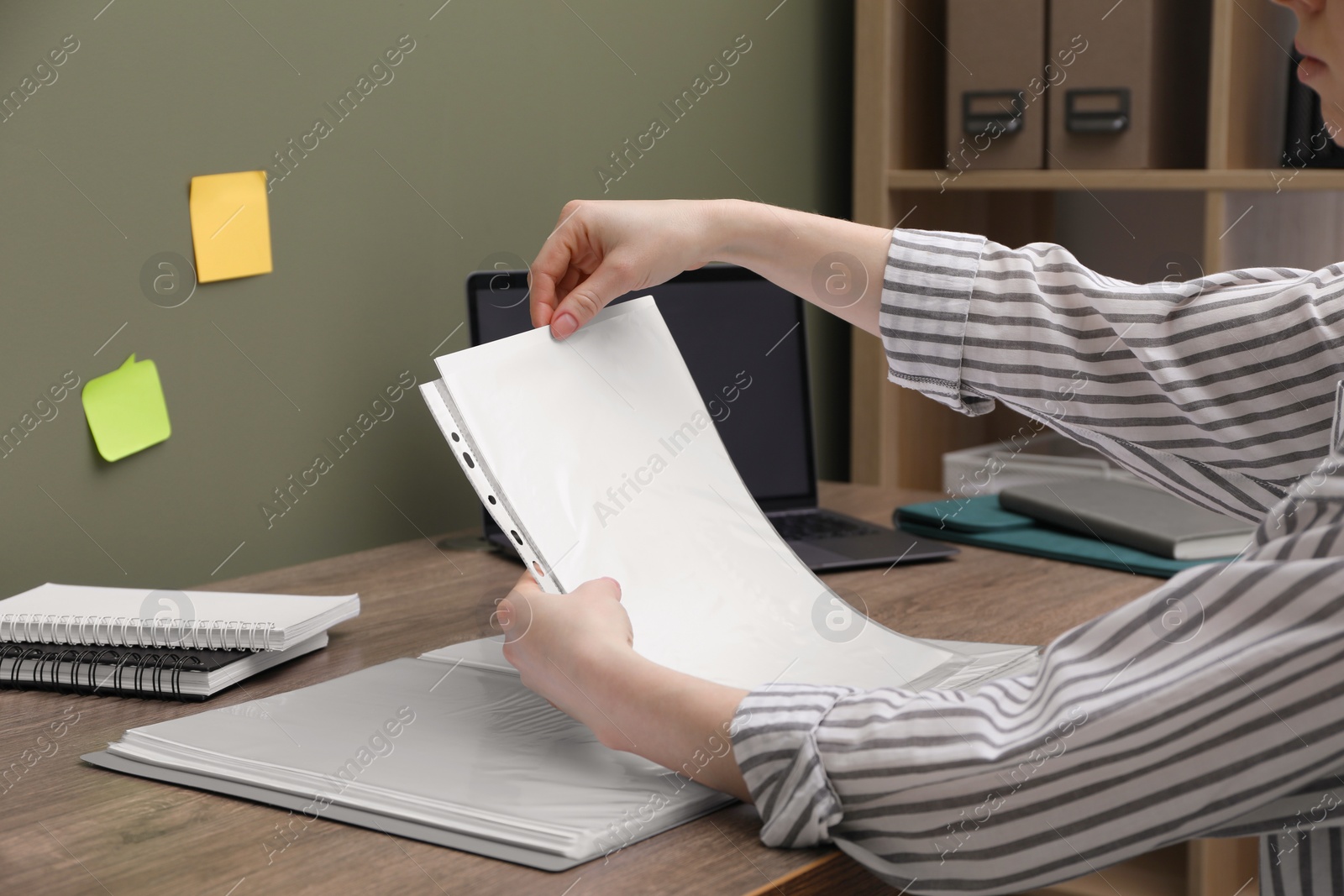 Photo of Woman putting paper sheet into punched pocket at wooden table, closeup