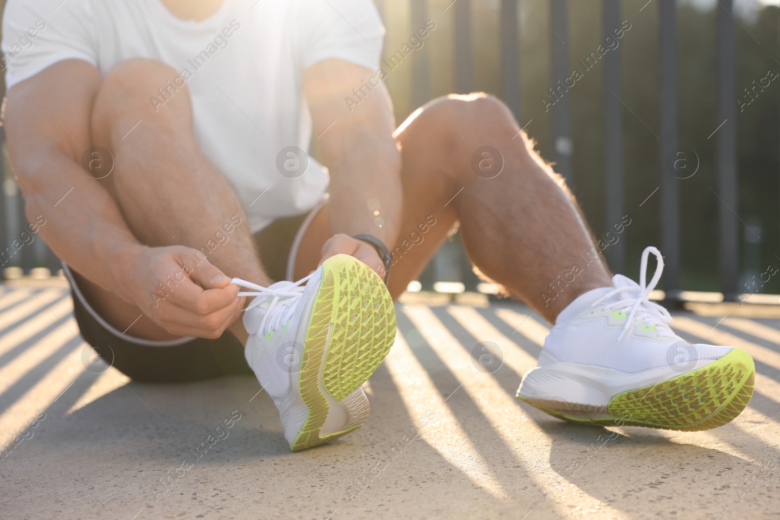 Photo of Man tying shoelaces before running outdoors on sunny day, closeup