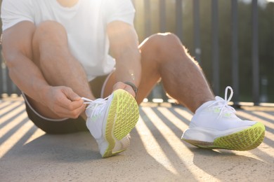 Photo of Man tying shoelaces before running outdoors on sunny day, closeup