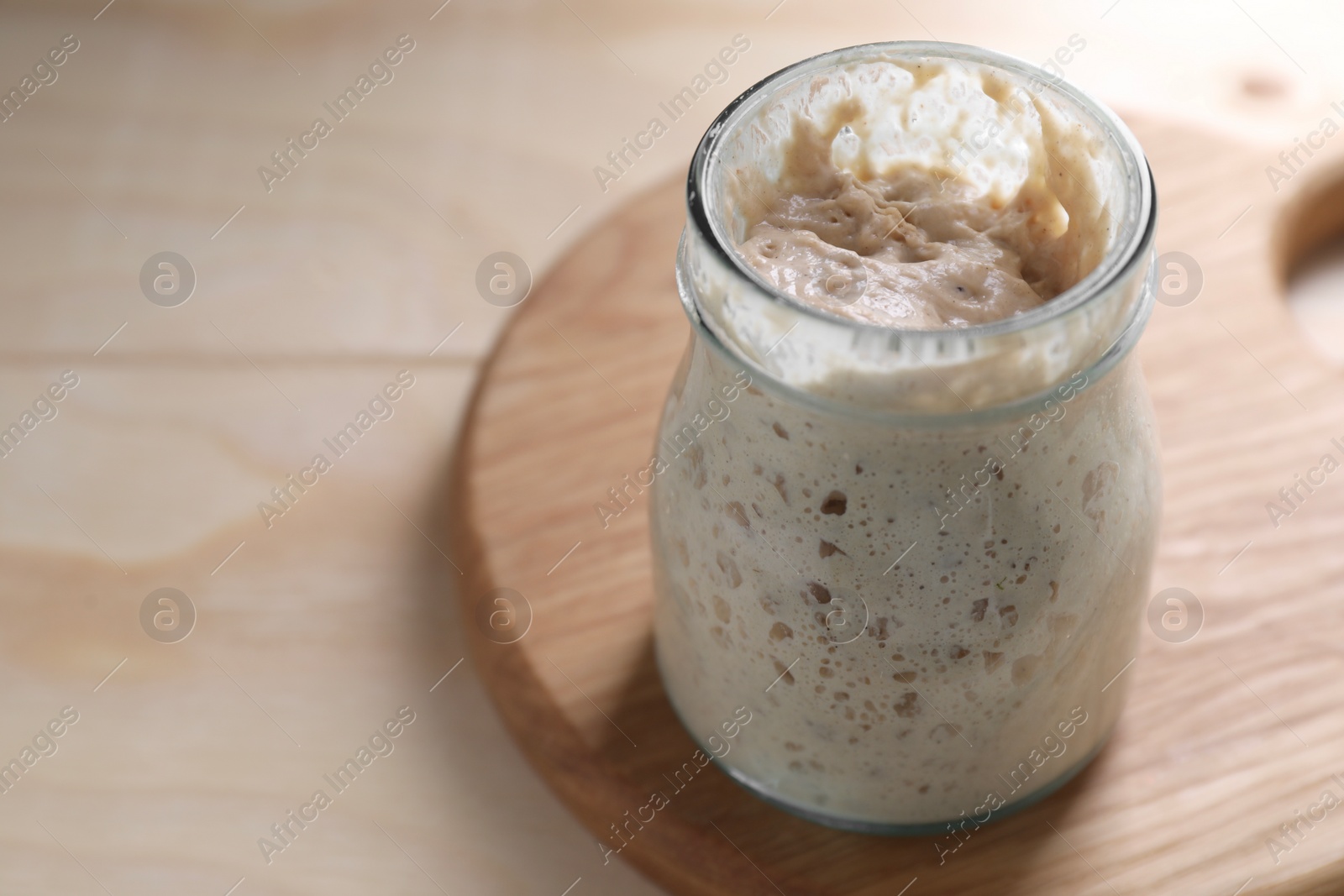 Photo of Sourdough starter in glass jar on wooden table, closeup. Space for text