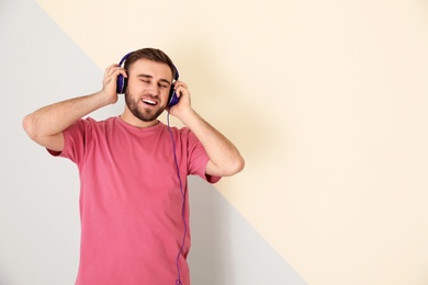 Photo of Handsome man enjoying music in headphones on color background. Space for text