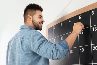 Young man writing with chalk on board calendar