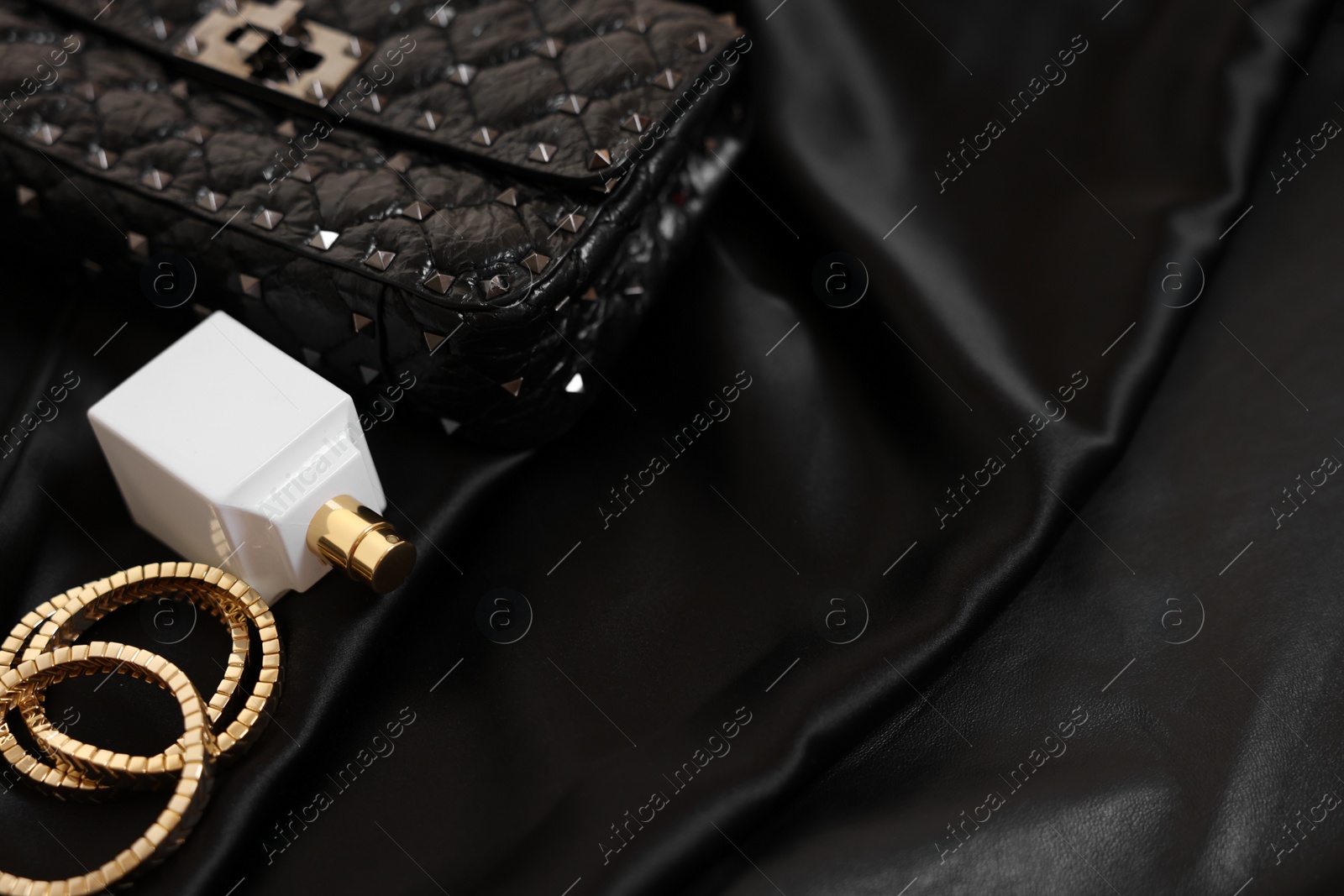 Photo of Leather bag, bottle of perfume and golden bracelets on black fabric, closeup. Space for text