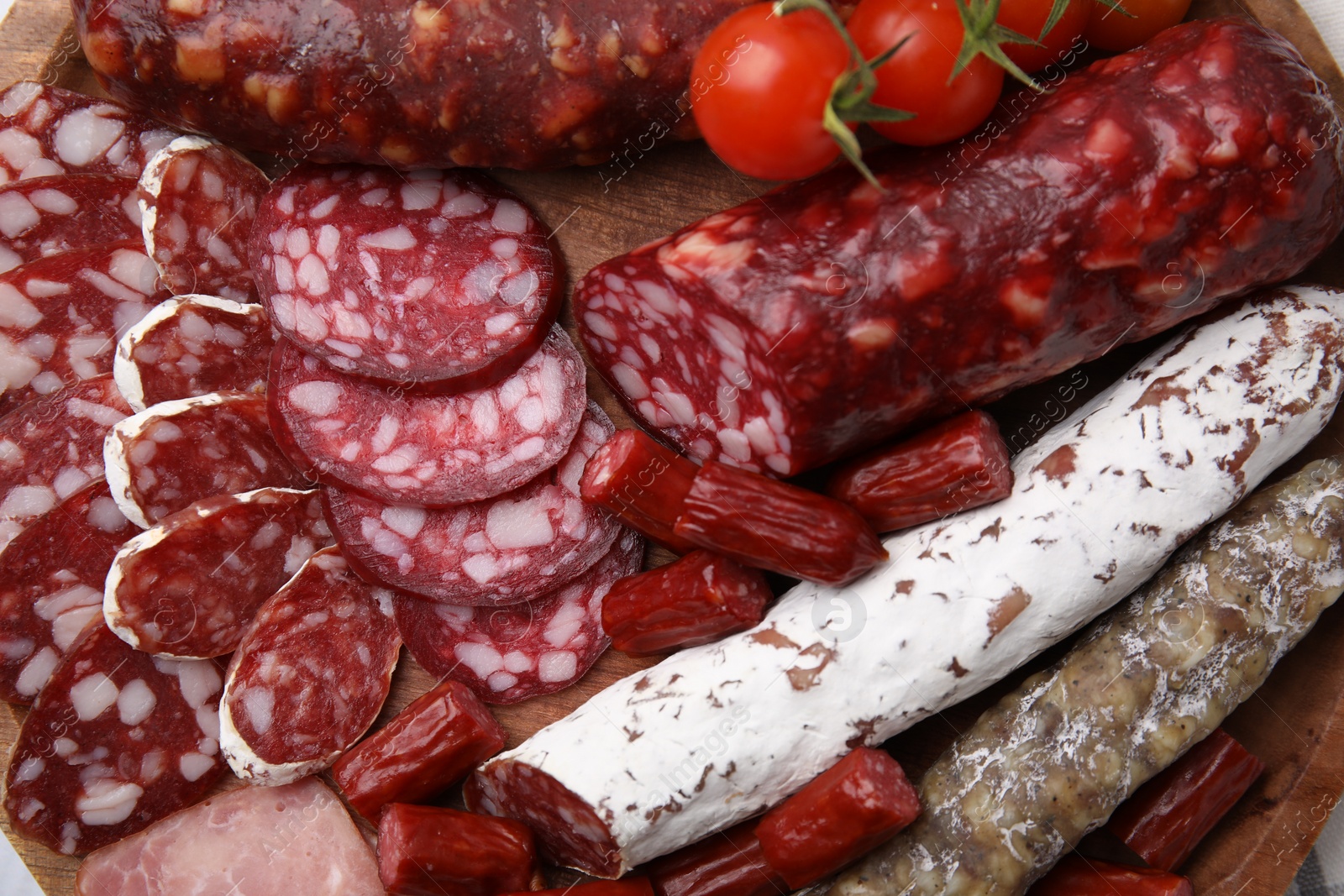 Photo of Different types of delicious sausages and tomatoes on wooden board, flat lay