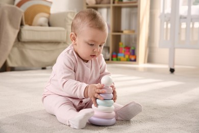 Cute baby girl playing with toy pyramid on floor at home