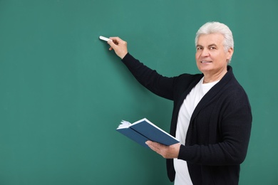 Portrait of senior teacher with book and chalk at green board, space for text