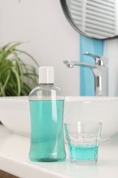 Photo of Bottle of mouthwash and glass on white table in bathroom