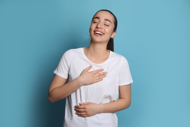 Beautiful young woman laughing on light blue background. Funny joke