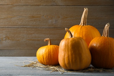 Photo of Ripe pumpkins on grey table against wooden background, space for text. Holiday decoration