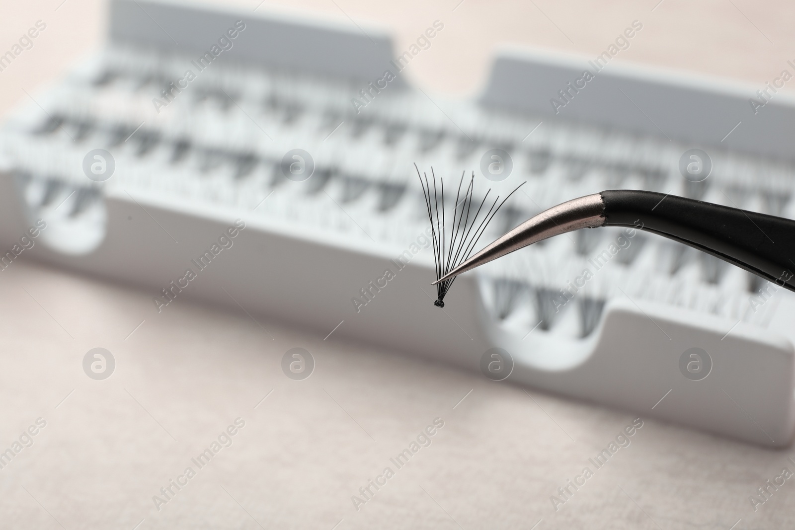 Photo of Tweezers with bunch of artificial eyelashes on blurred background, closeup. Space for text