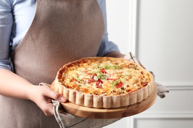 Photo of Woman holding board with tasty quiche indoors, closeup