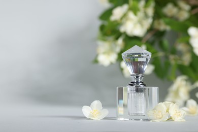 Photo of Aromatic perfume in bottle and beautiful jasmine flowers on grey background, space for text