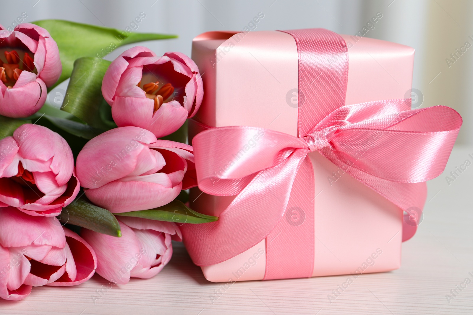 Photo of Beautiful gift box with bow and pink tulip flowers on white table, closeup