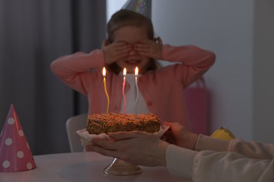 Birthday celebration. Mother holding tasty cake near her daughter indoors, focus on burning candles