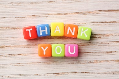 Photo of Phrase Thank You made of colorful cubes on light wooden table, top view