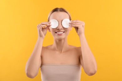 Smiling woman removing makeup with cotton pads on yellow background