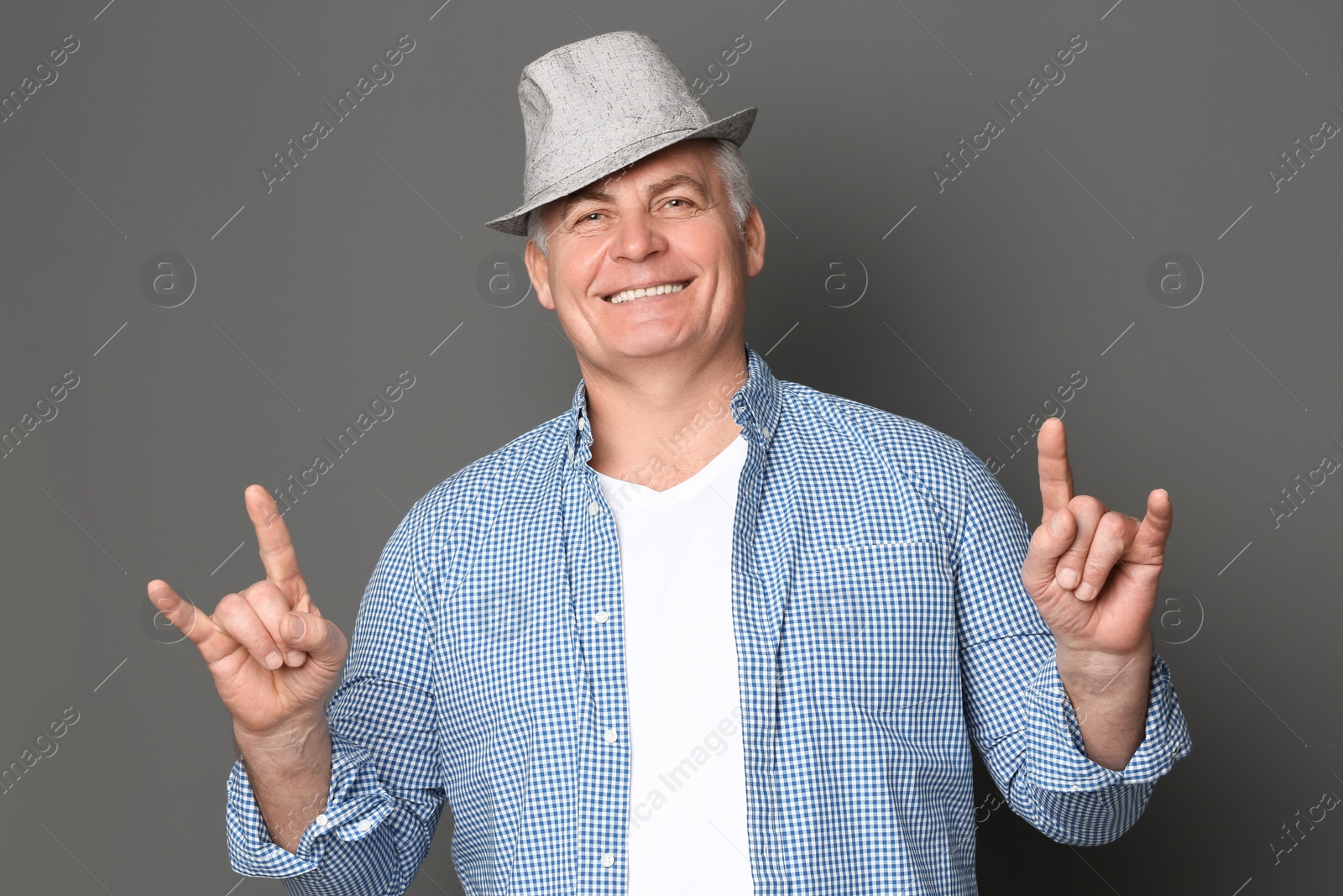 Photo of Portrait of stylish mature man showing devil horns sign with hands against grey background