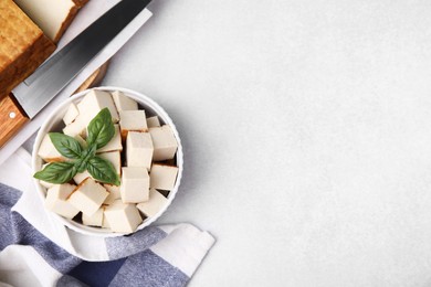 Bowl of smoked tofu cubes with basil and knife on white table, flat lay. Space for text