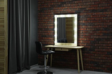 Photo of Mirror with light bulbs, table, chair and curtain in makeup room