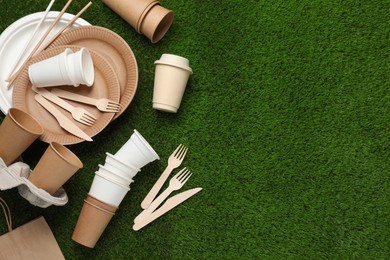 Photo of Eco disposable tableware on green artificial grass, flat lay. Space for text