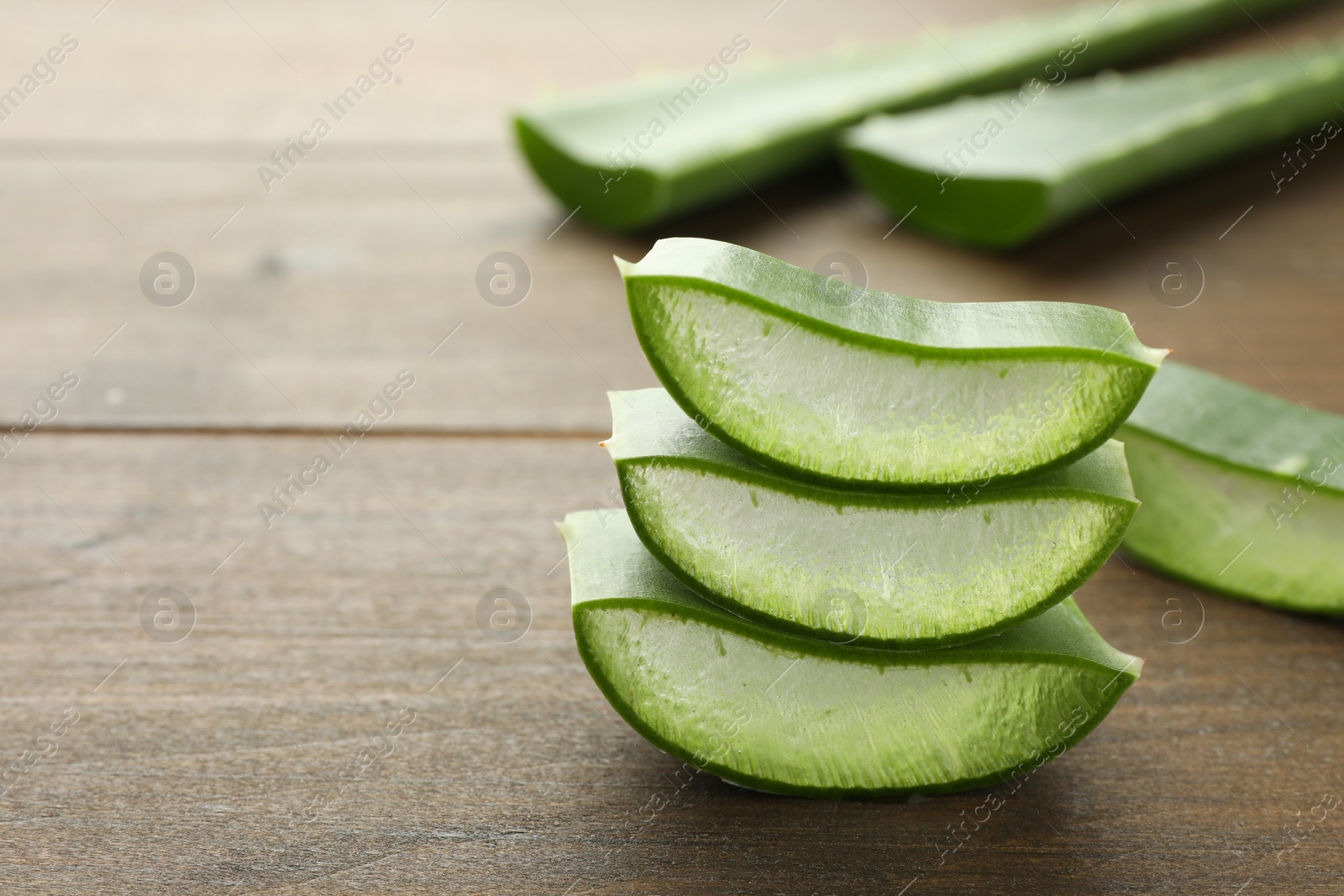 Photo of Fresh aloe vera pieces on wooden table, closeup. Space for text