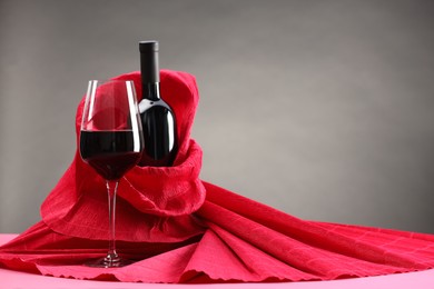 Photo of Stylish presentation of delicious red wine in bottle and glass on pink table against grey background. Space for text