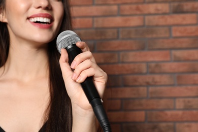 Young woman singing in microphone near brick wall, closeup view with space for text