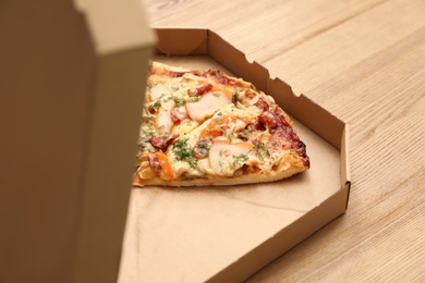Photo of Cardboard box with pizza pieces on wooden table. Space for text