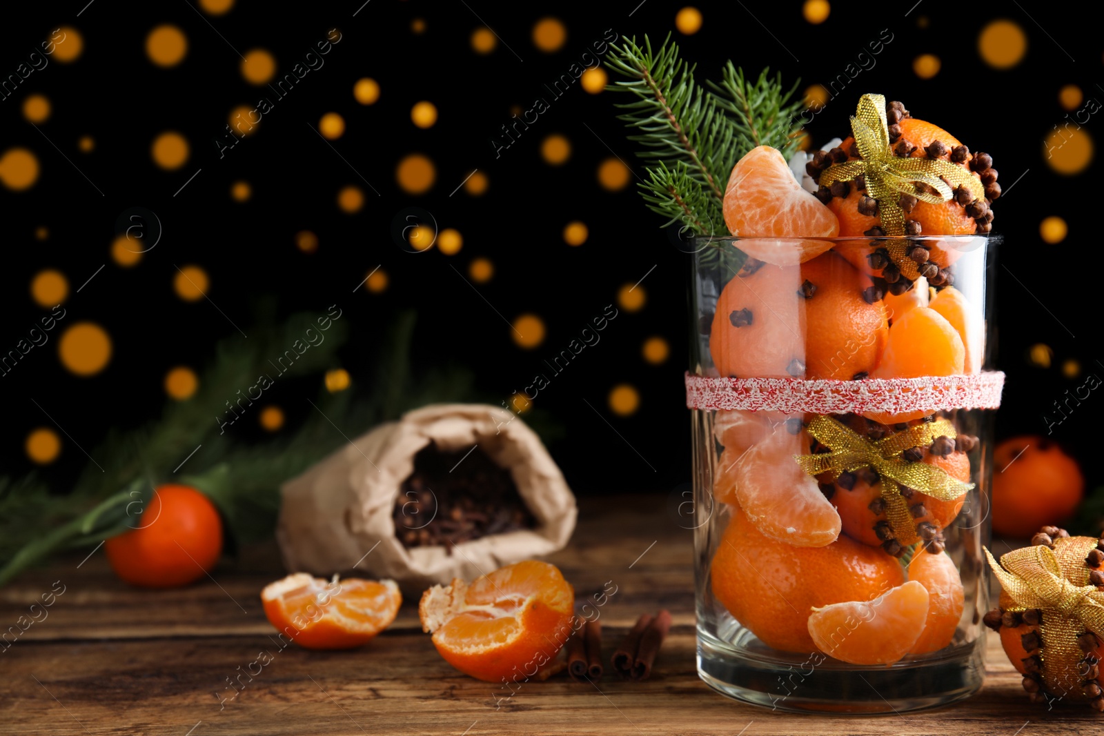 Photo of Christmas composition with tangerine pomander balls in glass on wooden table against blurred lights
