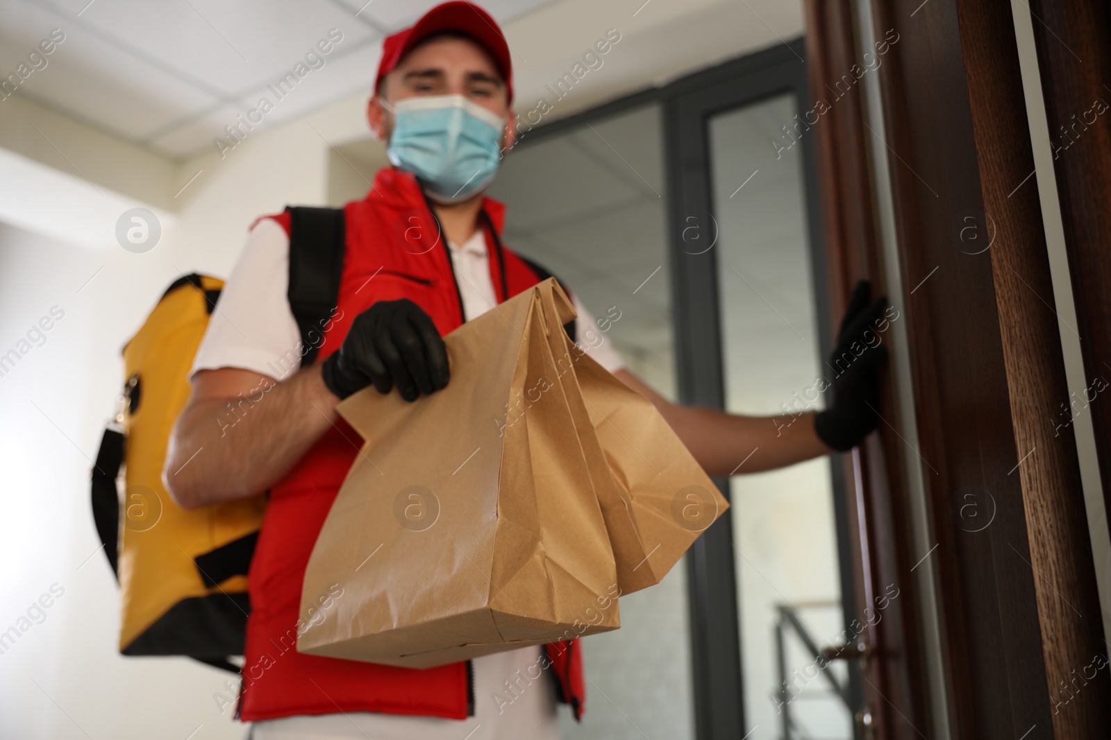 Photo of Courier in protective mask and gloves with order at entrance, focus on hands. Restaurant delivery service during coronavirus quarantine