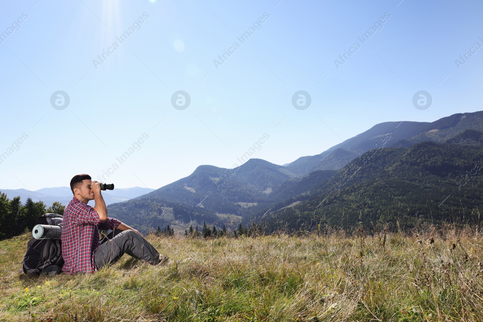 Photo of Tourist with hiking equipment looking through binoculars in mountains