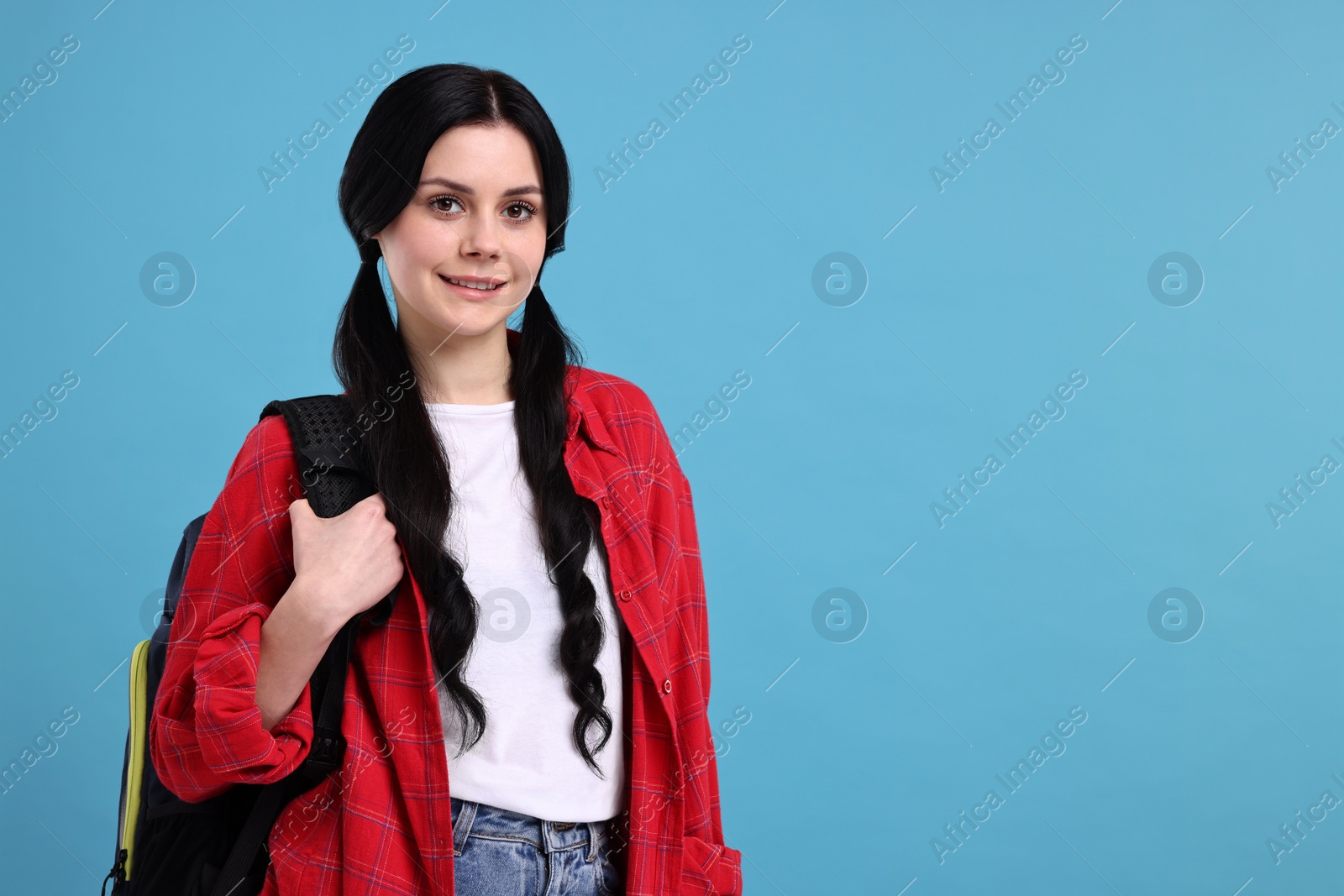 Photo of Smiling student with backpack on light blue background. Space for text